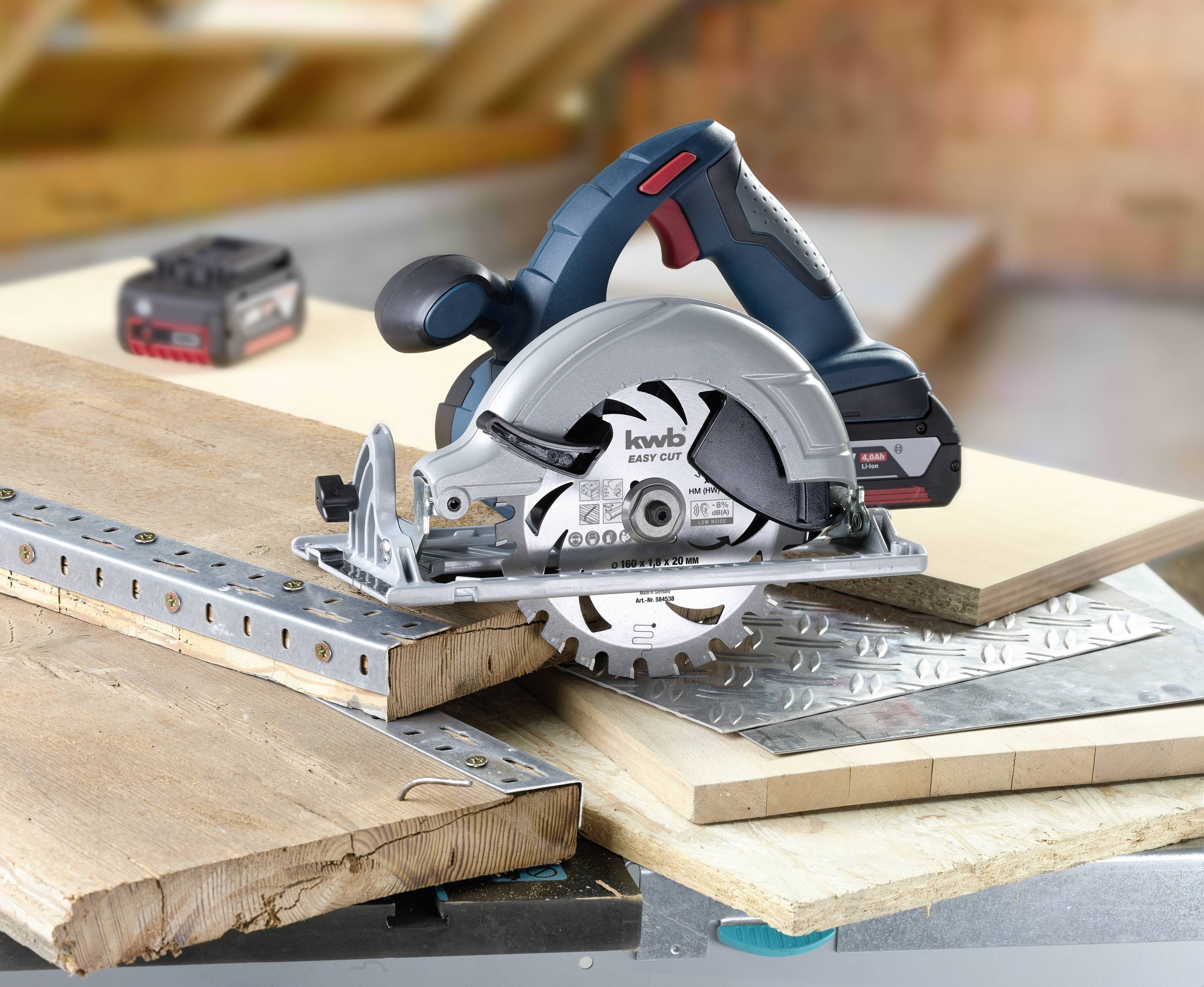Battery-powered circular saw cutting a wooden board. Further tools and building materials are visible in the background.