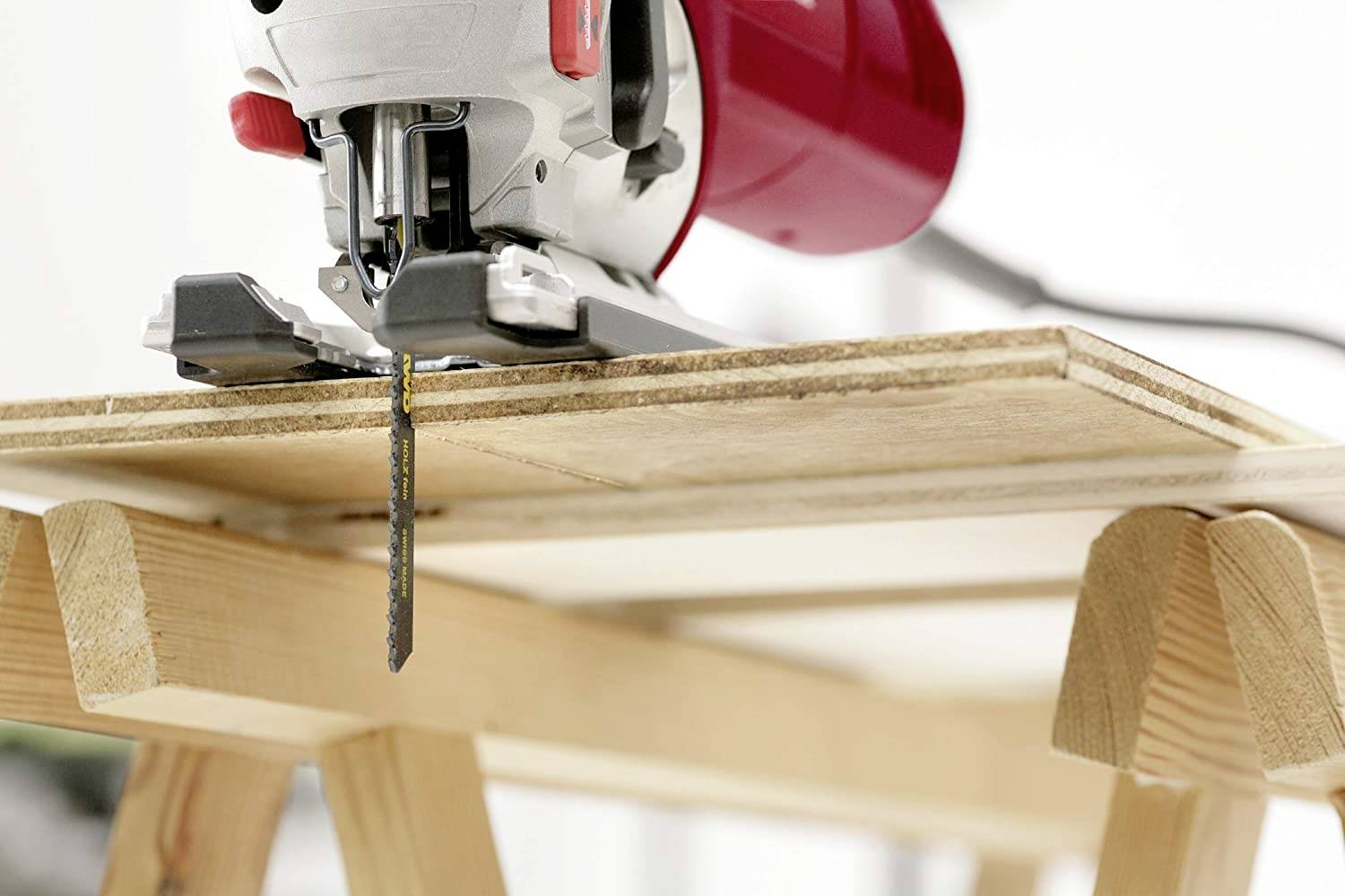 A jigsaw cuts through a wooden board lying on a sawhorse. Blurred background, focus on the saw.