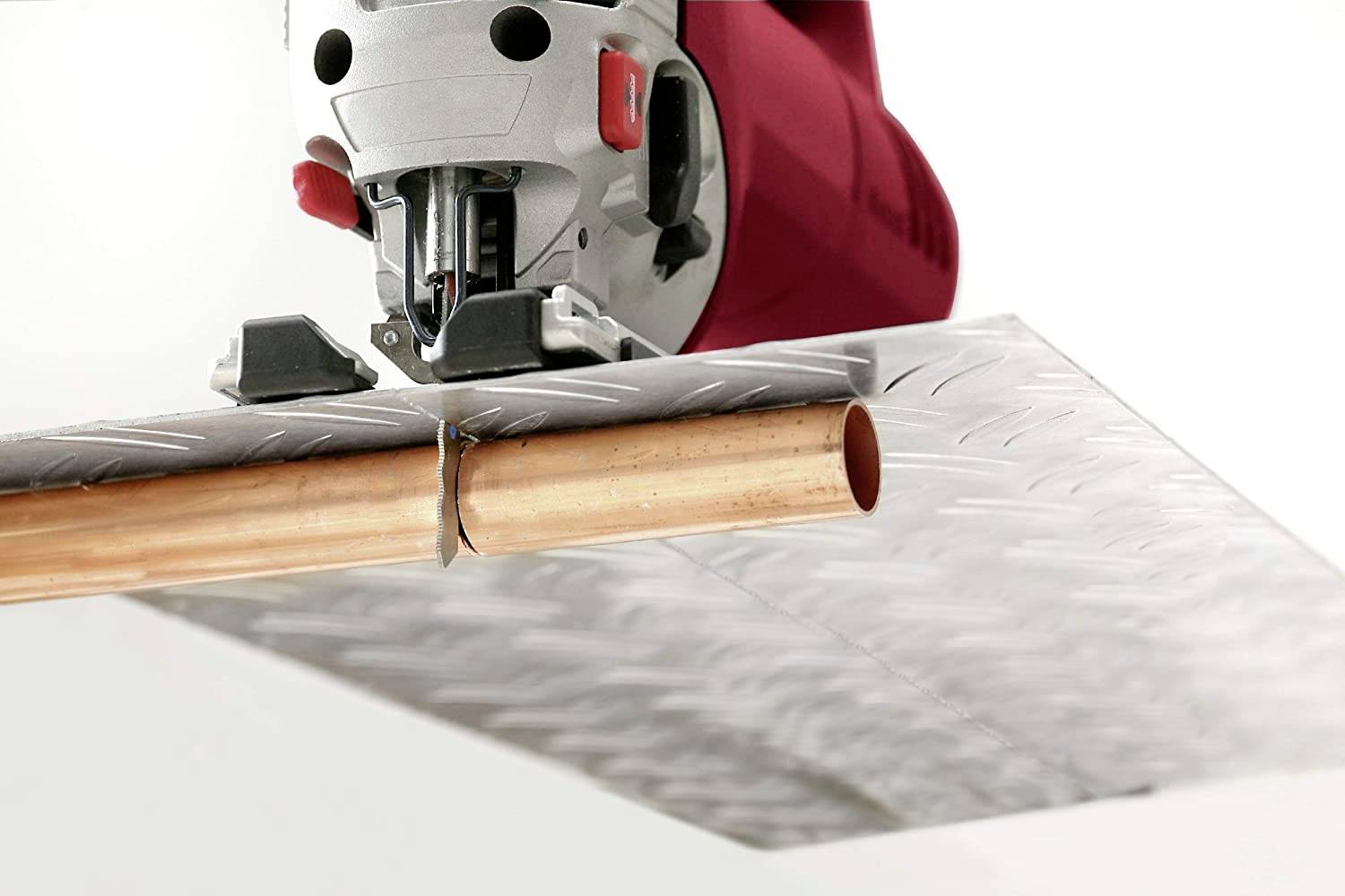 An electric tool is cutting a copper pipe lying beneath a metal plate.