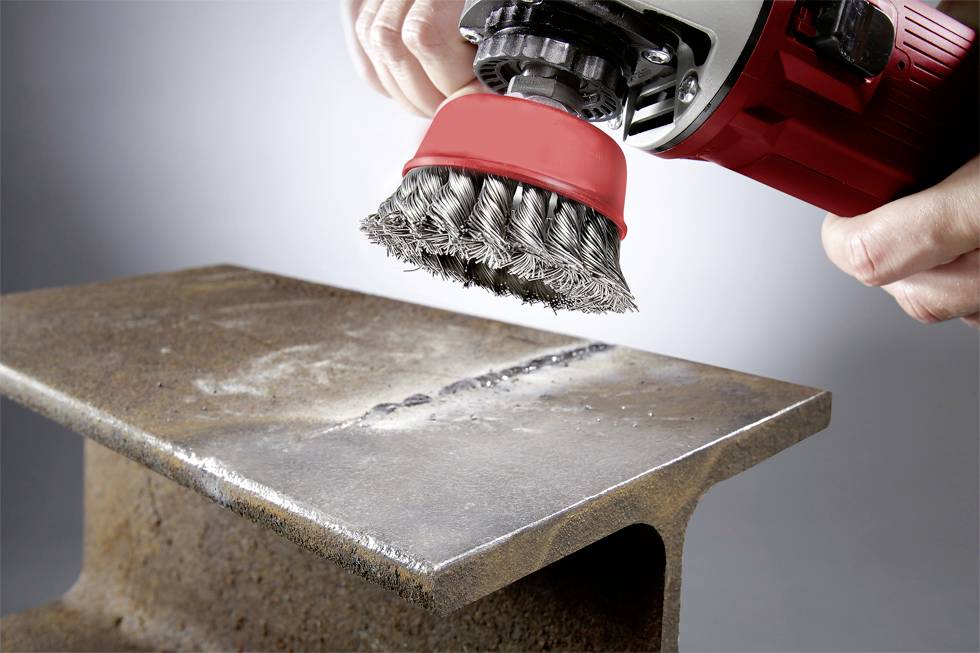 A person is using a red and black grinding machine to remove rust from a large piece of metal.