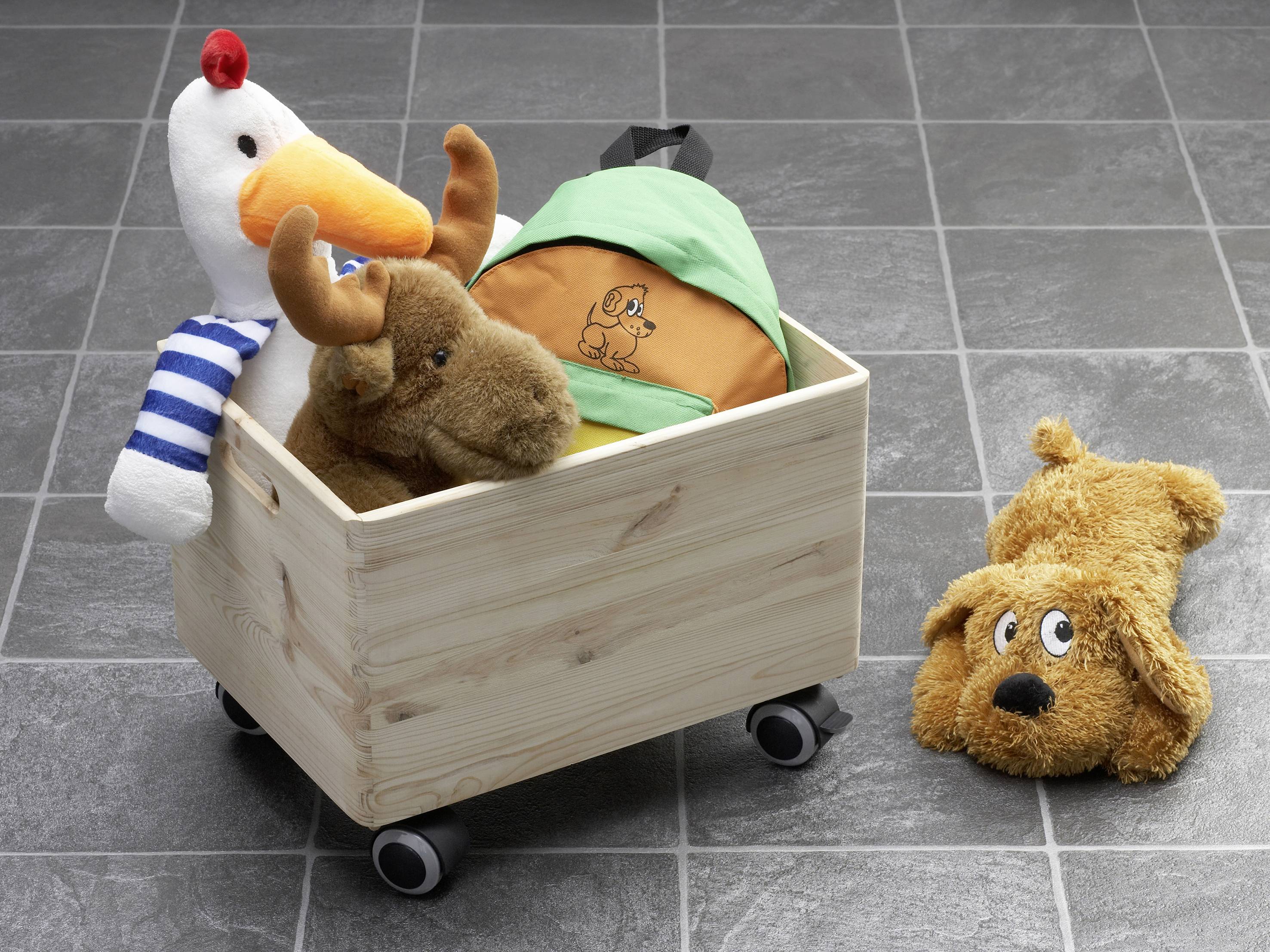 A wooden box on wheels is filled with a plush elk and a soft toy in a tent. A stuffed dog lies beside it on the floor.