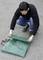 A man is kneeling outside and folding a green tarpaulin on an asphalt surface.