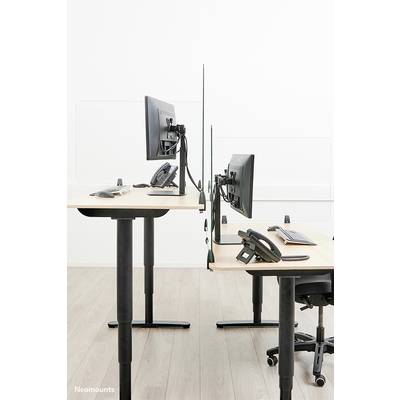 Two height-adjustable desks with monitors and telephones, separated by a transparent partition, on a wooden floor.