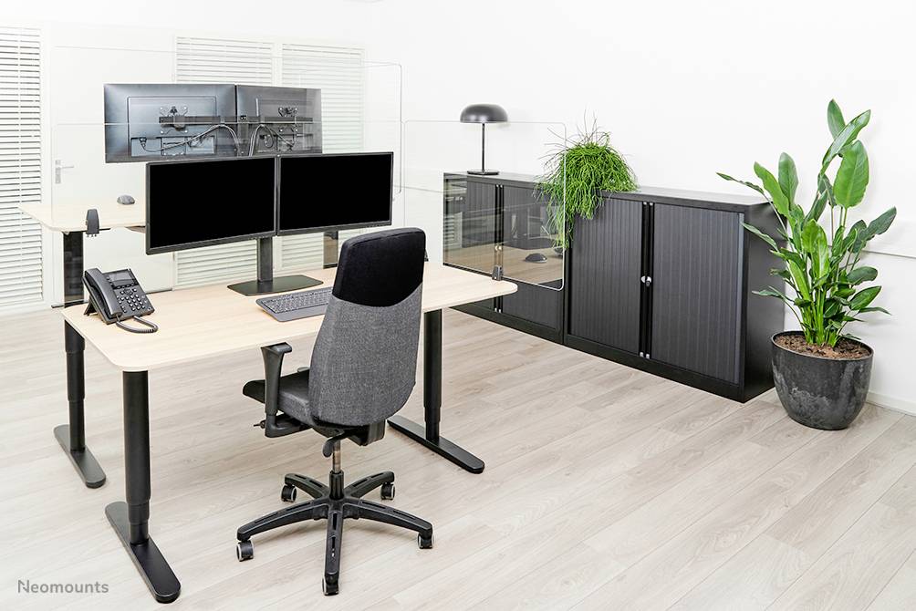 A modern office with an adjustable-height desk, two monitors, a chair, a plant, and a black cabinet.