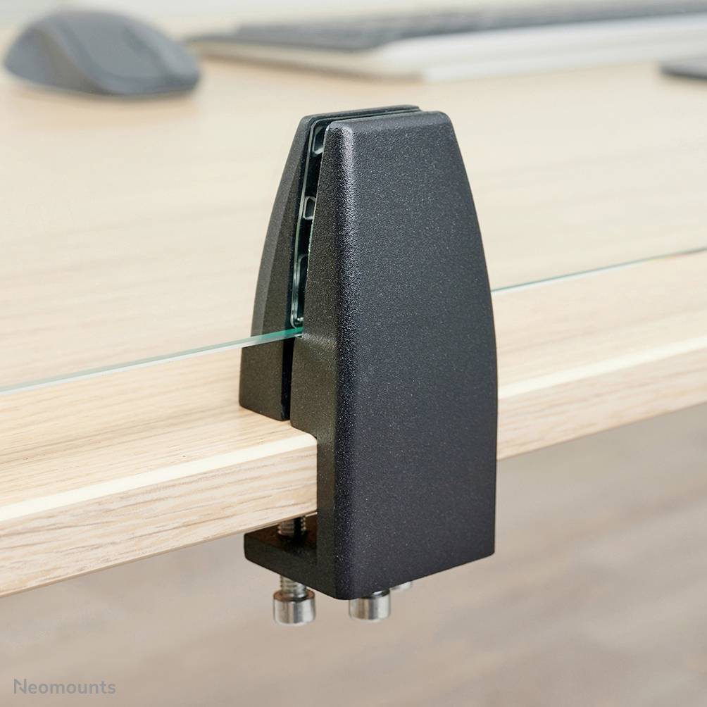 Black mounting bracket on a glass table, attached to the table edge. Background shows blurred table surface and part of a mouse.
