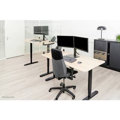 Two modern workstations with height-adjustable desks, monitors, keyboards and office chairs in a bright office.