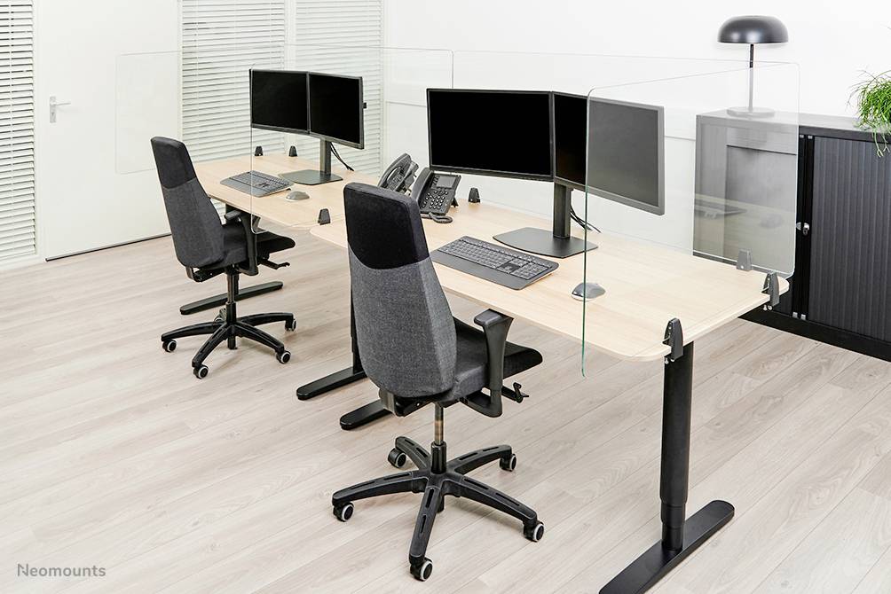 Two modern workstations with monitors, keyboards and office chairs on light laminate flooring, separated by glass partitions.