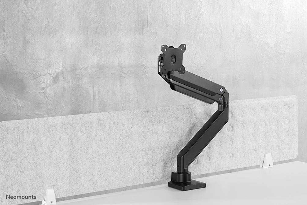 A black metal monitor arm is mounted on a white table in front of a grey wall.