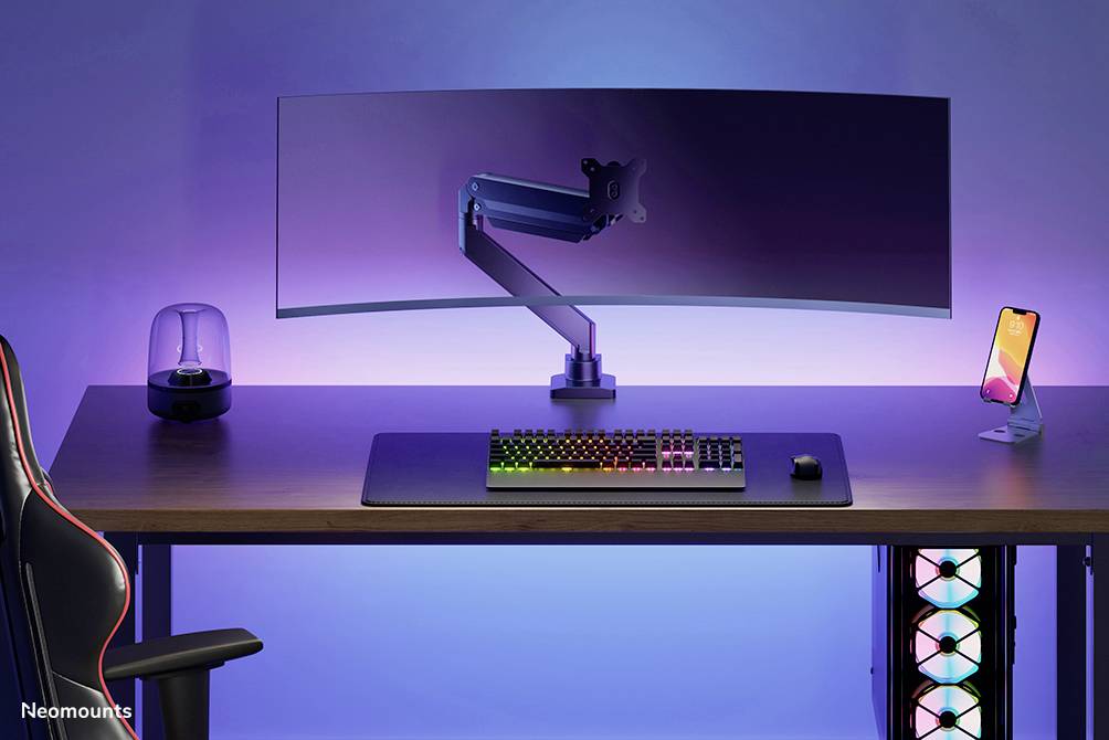 A modern desk with a curved monitor, backlit keyboard, mouse, mobile phone holder, speakers, and illuminated computer tower.