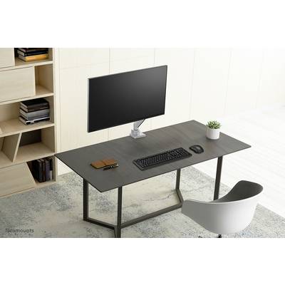 A tidy desk with a monitor, keyboard, mouse and a notebook. In the background, a bookshelf with books; a modern, minimalist interior.
