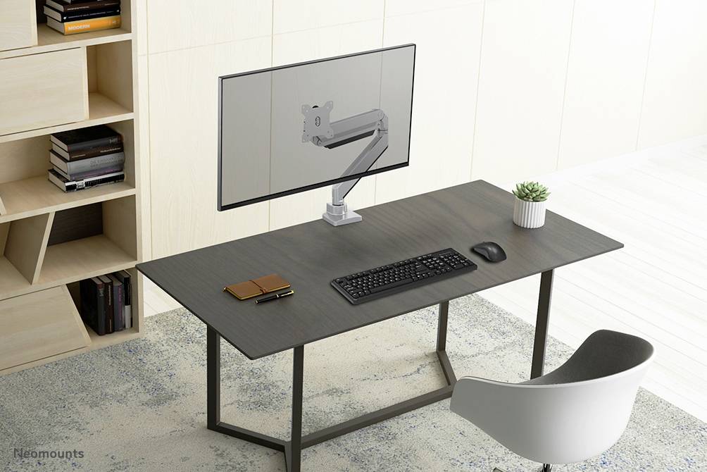 A modern desk with a monitor arm, on which a screen is mounted. A keyboard and mouse are placed on the desk, along with a small plant pot.