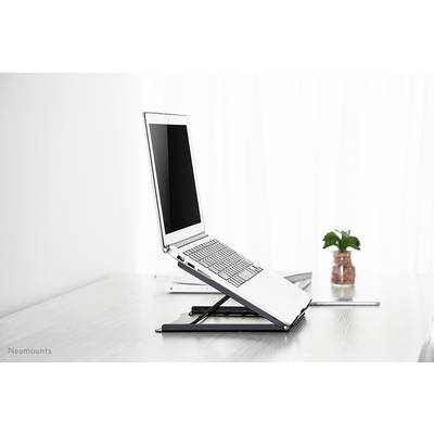A laptop is positioned on an adjustable stand on a desk. A plant is visible in the background.