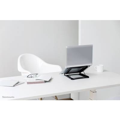A laptop on an adjustable-height stand sits on a desk. Beside it are a pair of glasses, books, and a mug.