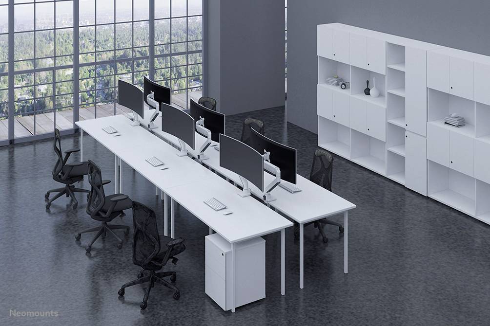 Modern office space with long desks, ergonomic chairs, and multiple computer monitors. Large windows overlooking woodlands.