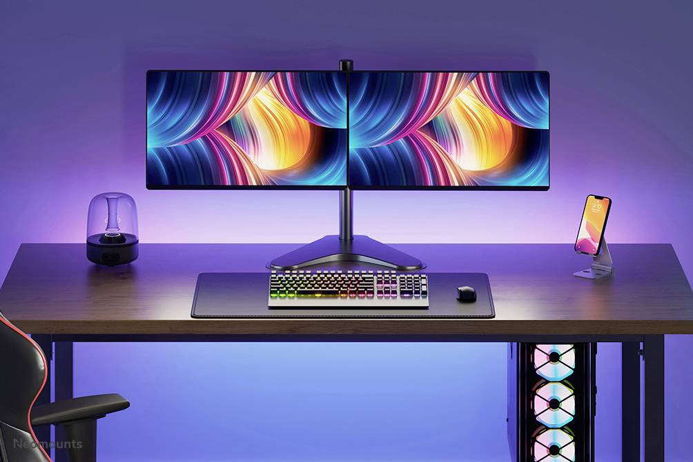 A modern desk with dual monitors displays colourful abstractions. An illuminated keyboard and mouse are centrally positioned.
