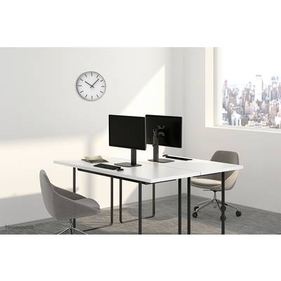 A modern office with two computer monitors on a white desk, two grey chairs, a wall clock, and a window view of a city.
