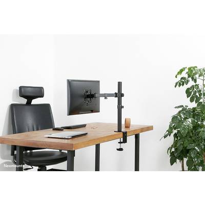 A modern desk with an office chair, a laptop, a screen on an arm, and a plant on the right.