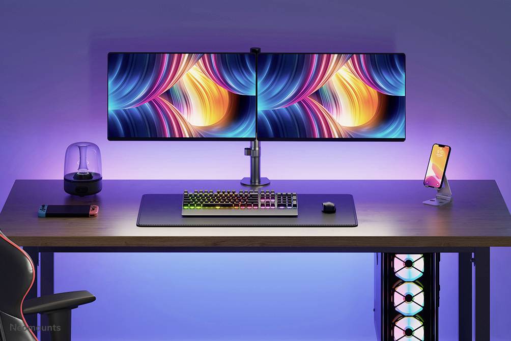A desk with two large monitors, a colourful keyboard, a mouse, and a smartphone on a stand. Colourful LED lighting in the background.