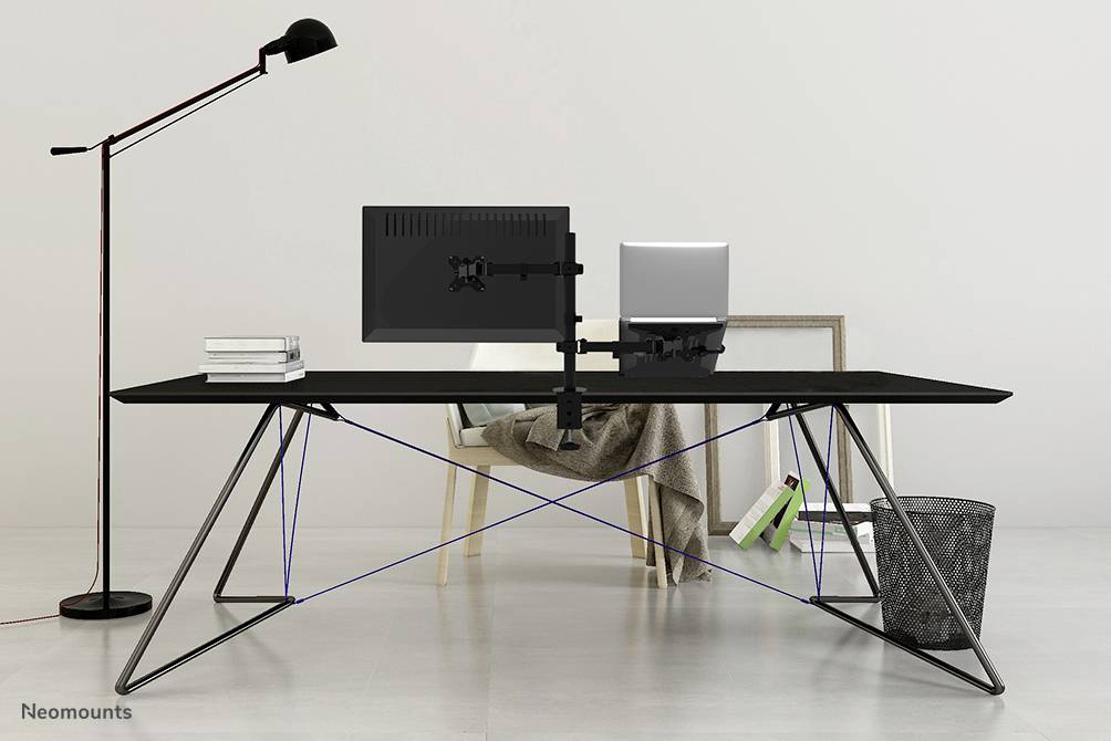 A modern desk with a monitor, a laptop, books and a desk lamp. In the background, a chair and a wastepaper bin.