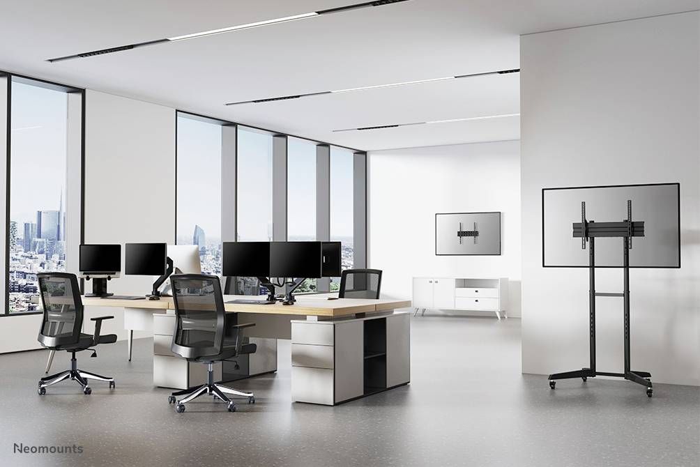 A modern office with desks, multiple monitors and chairs positioned in front of large windows overlooking a cityscape.