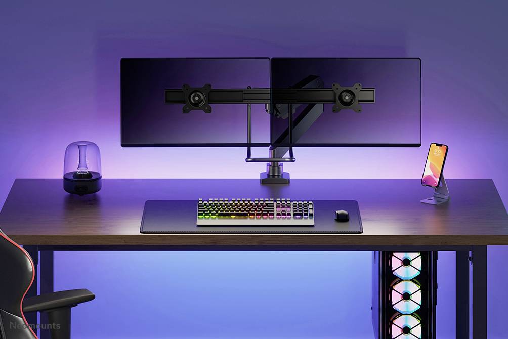 A modern workspace with two monitors on a desk, an RGB keyboard and a smartphone in a holder; clear and organised layout.
