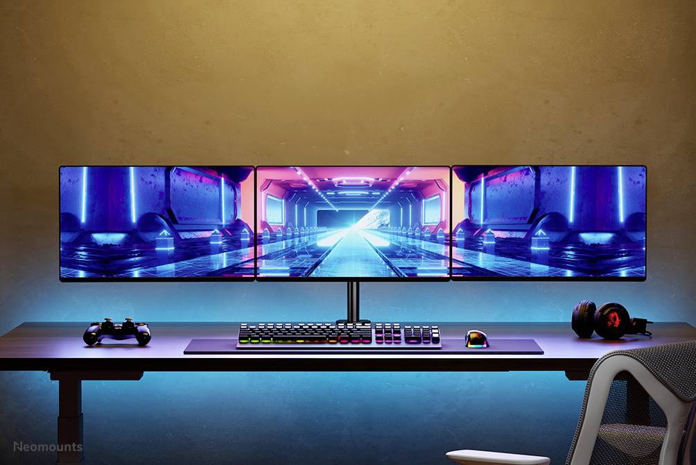 A gaming desk with three monitors displays a futuristic game. Beneath it are a keyboard, mouse, and headphones set against an illuminated background.