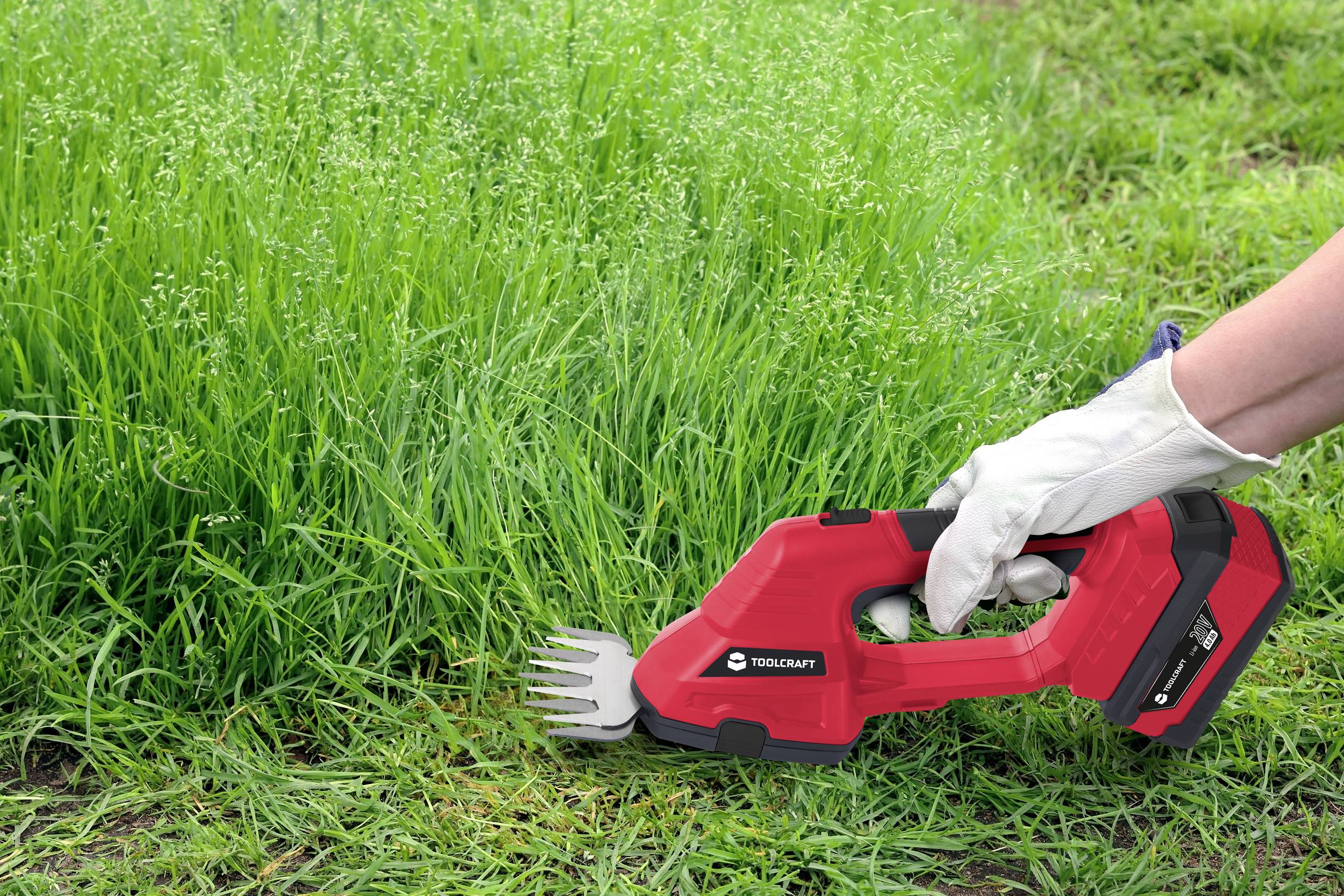 A hand is cutting dense grass with a red electric grass trimmer.