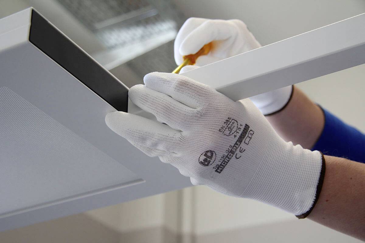A person wearing white gloves is installing a cooker hood with a screwdriver. Hands are working on the mounting.