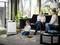 'A child is playing on the floor, while two adults sit on a sofa drinking coffee. Next to them stands an air purifier.'