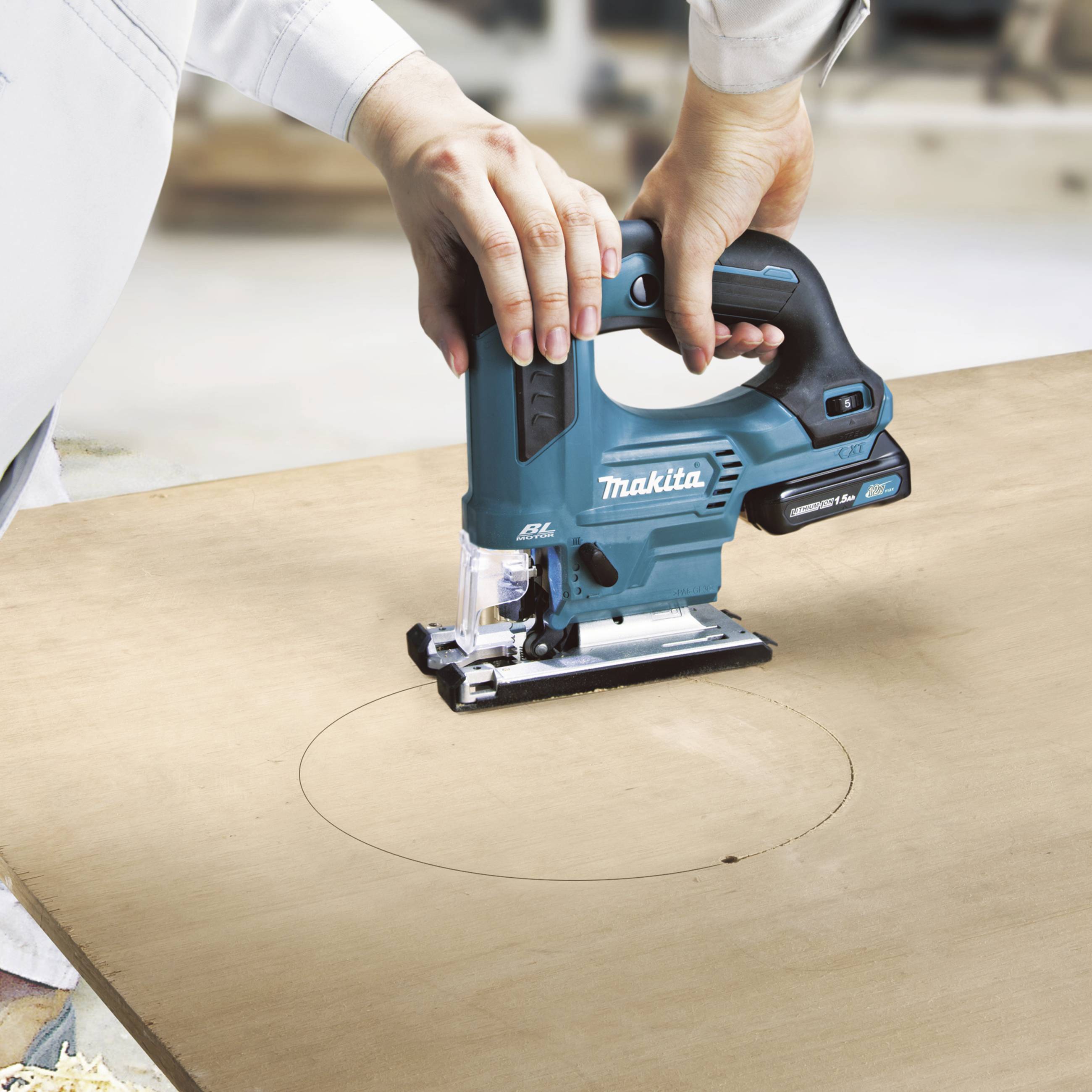 A person is using a blue jigsaw to cut a circular shape out of a wooden board.