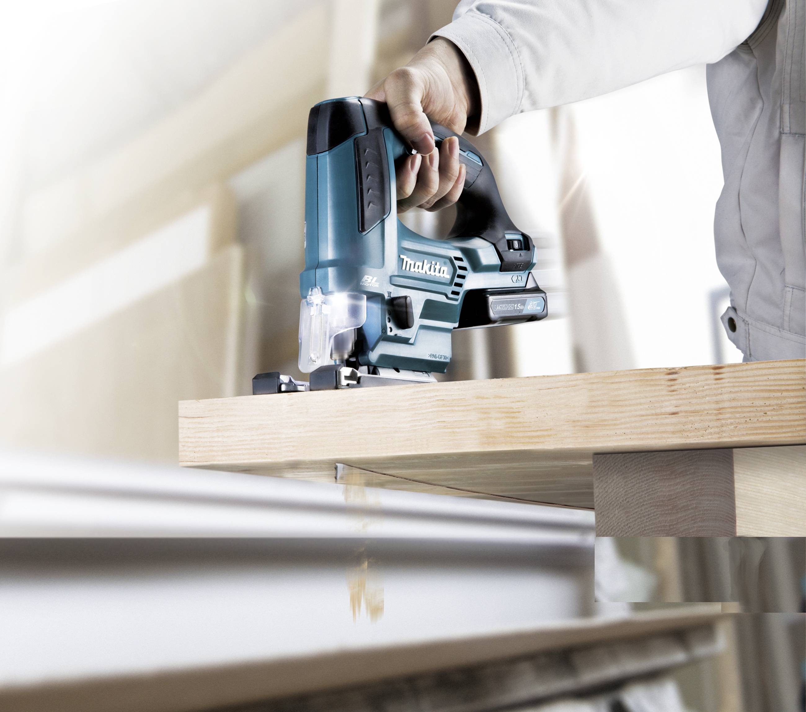 A person is using an electric jigsaw to cut a wooden board. The focus is on the saw and the board being sawn.