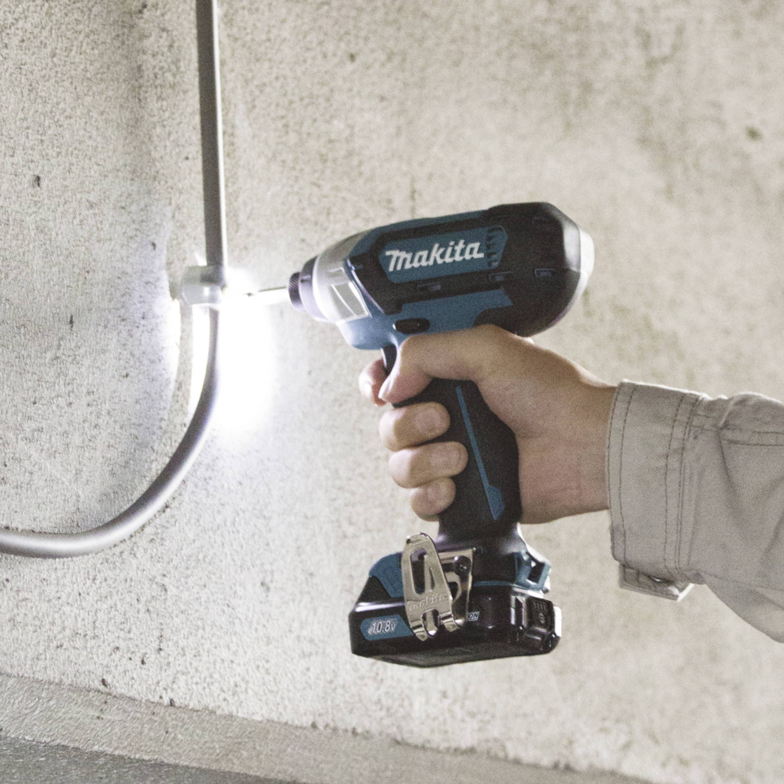 A person is using a blue cordless drill to screw a screw into a wall. A grey cable runs parallel to the wall.