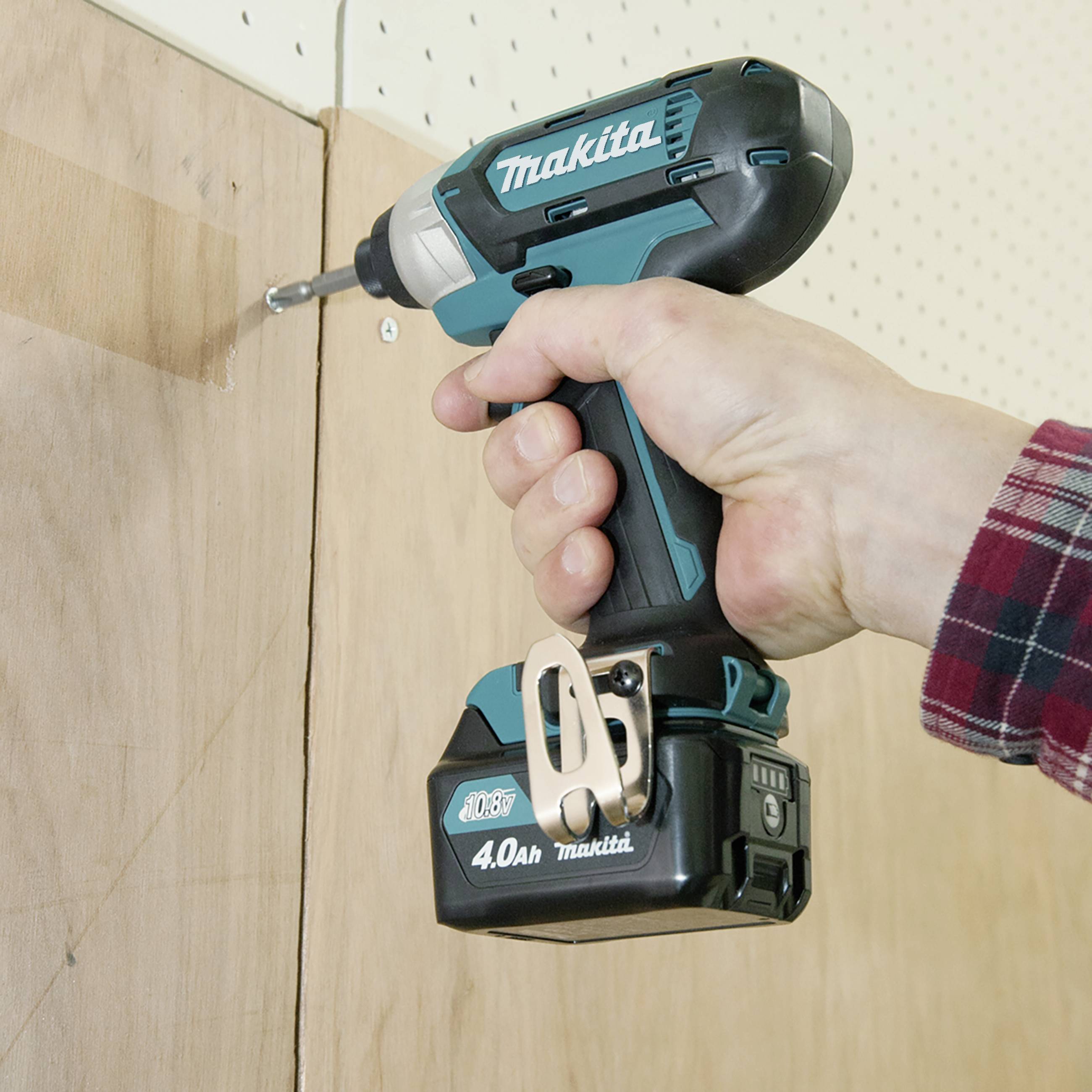 A person is holding a cordless drill and drilling a hole in a wooden board. The drill is a Makita brand.