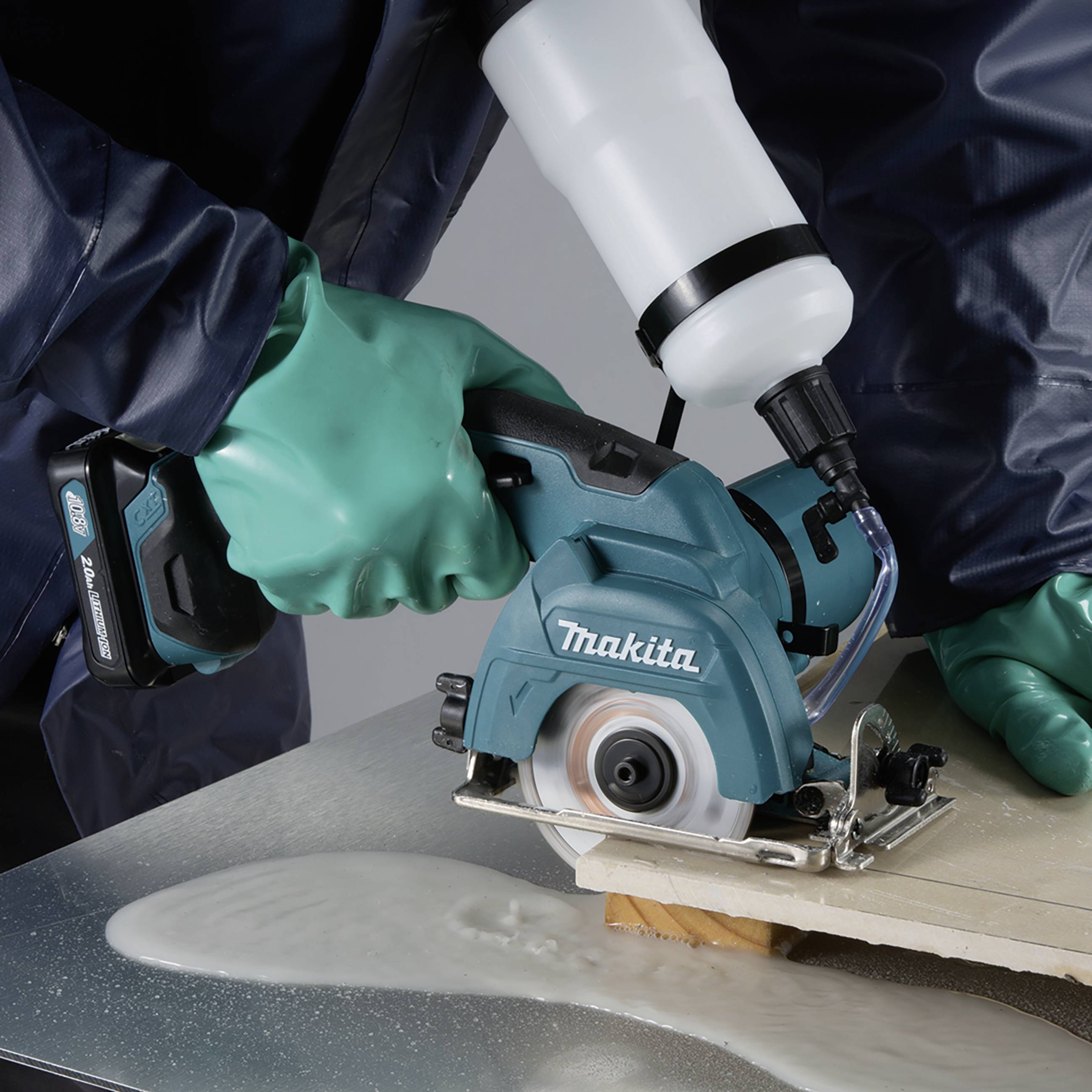 A person wearing green gloves is cutting a plank with a blue circular saw while it lies on a table.