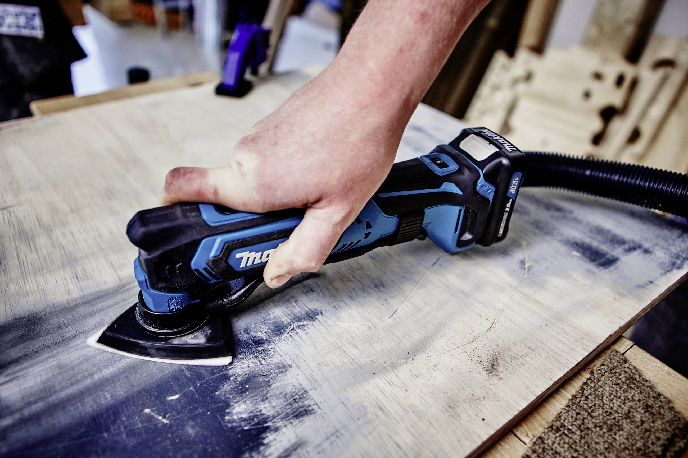A person is using a blue-black electric grinding tool on a wooden board to process the surface.