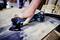 A person is using a blue-black electric grinding tool on a wooden board to process the surface.