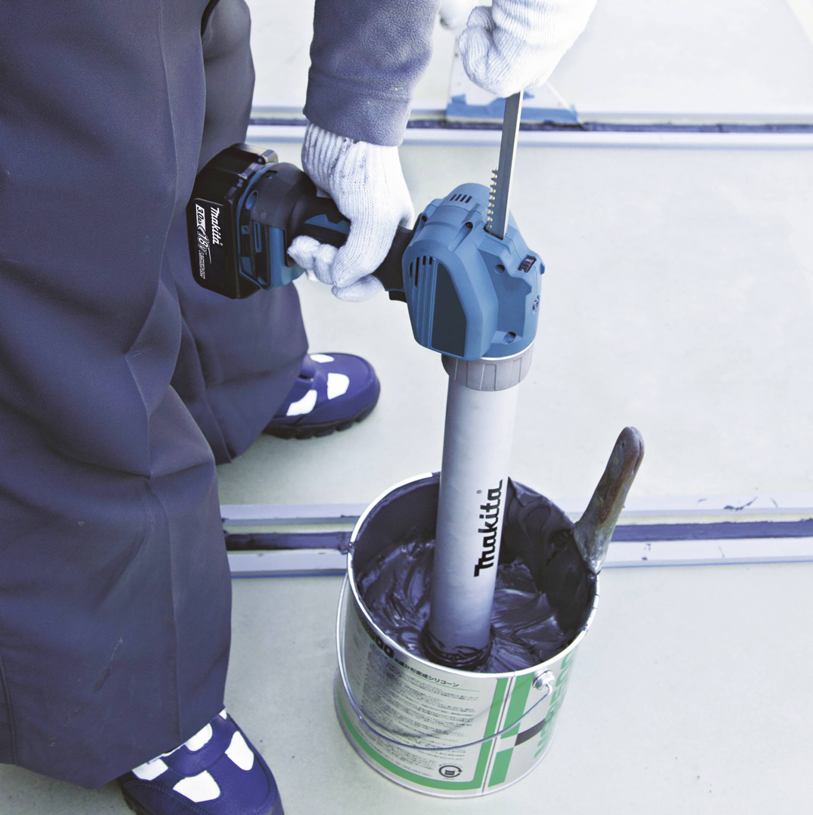 A person is mixing viscous material in a bucket using an electric mixing tool. Focus on the tool in use.