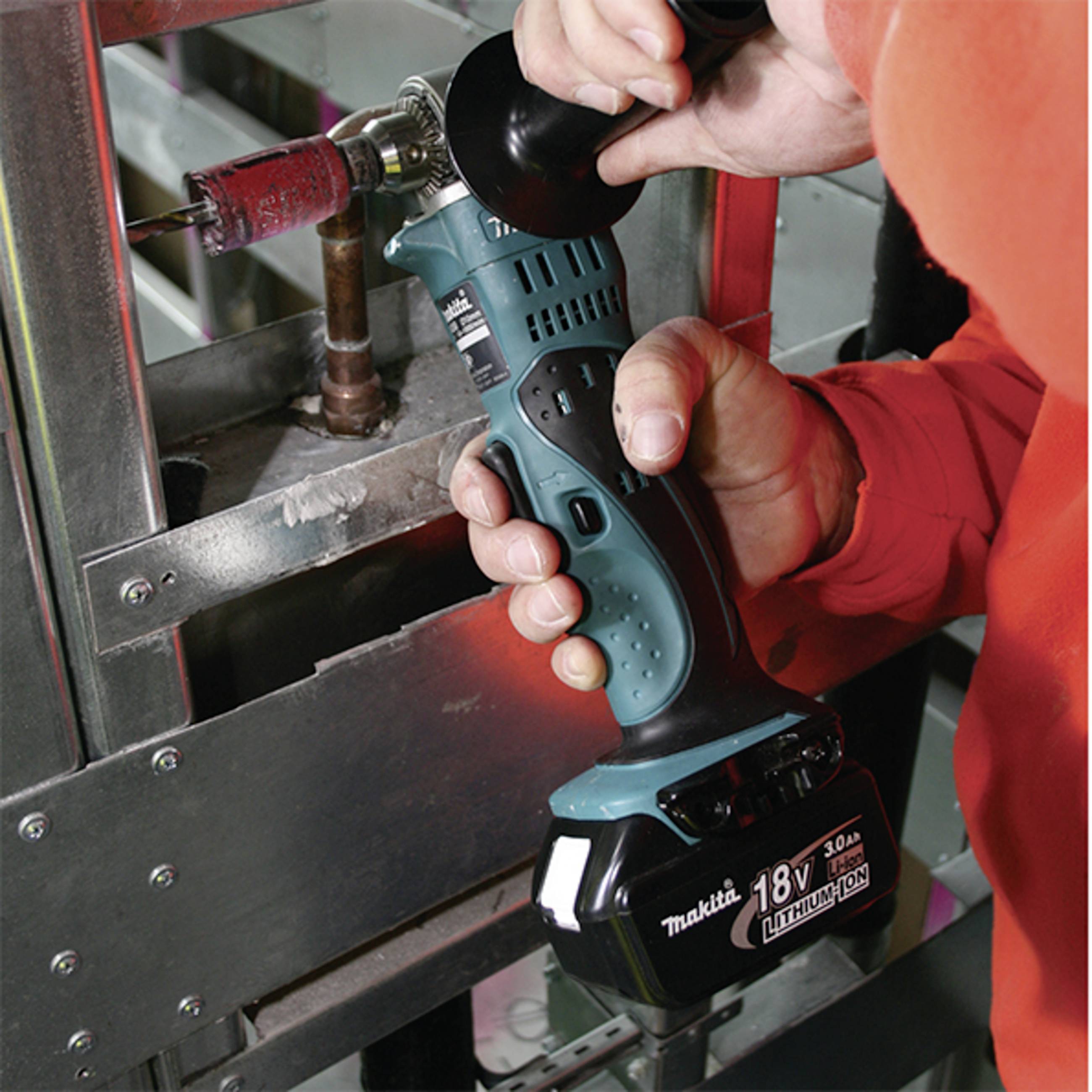A person is drilling a metal pipe with a cordless 18V drill. The drill is blue-black and is being used on a copper pipe.