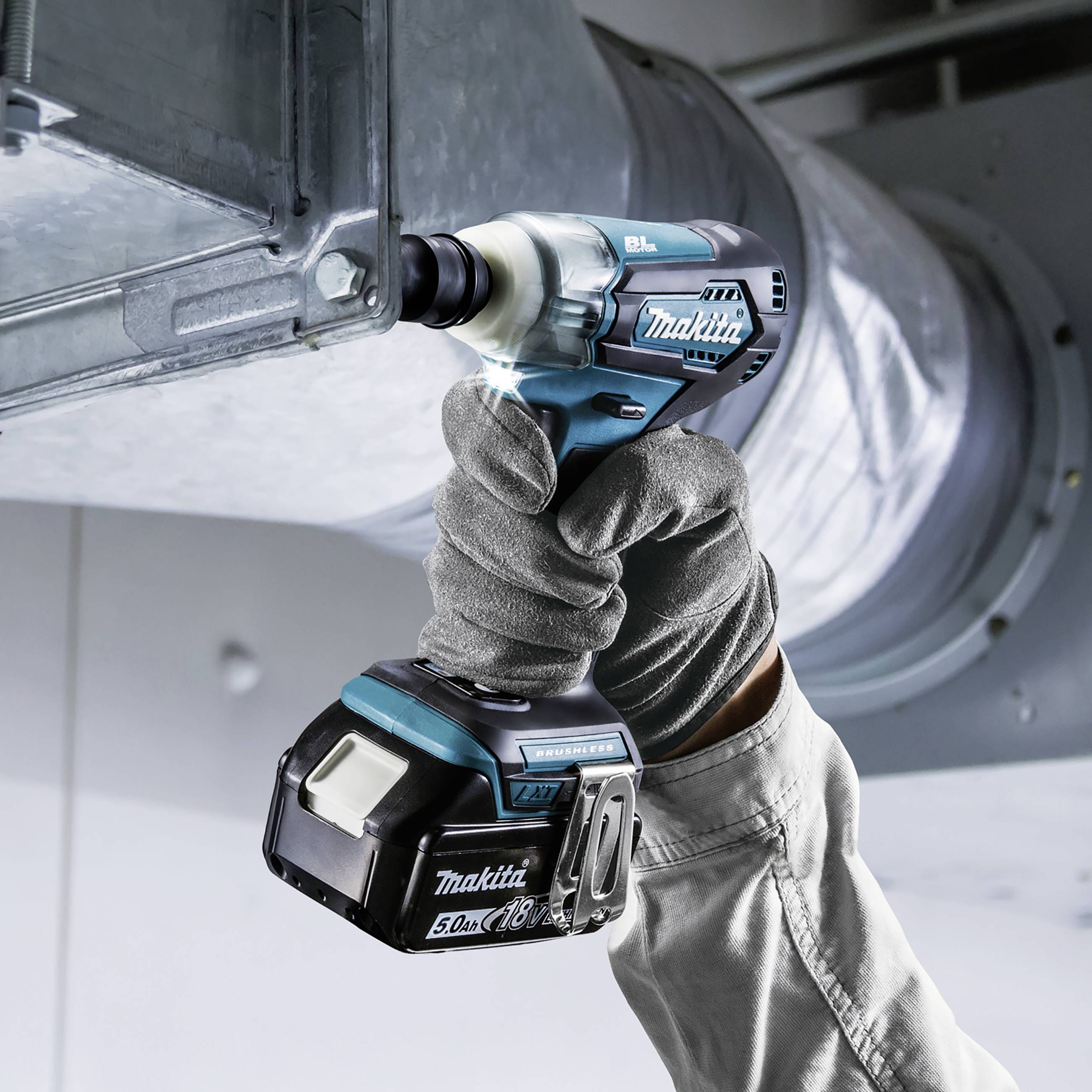 A cordless drill is being used by a worker wearing a glove to screw a bolt into a large metal pipe.