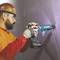 A person in work attire is using an electric tool to drill a screw into the wall.