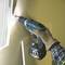 A person is using a cordless drill to screw a screw into the wall. The scene is well-lit.