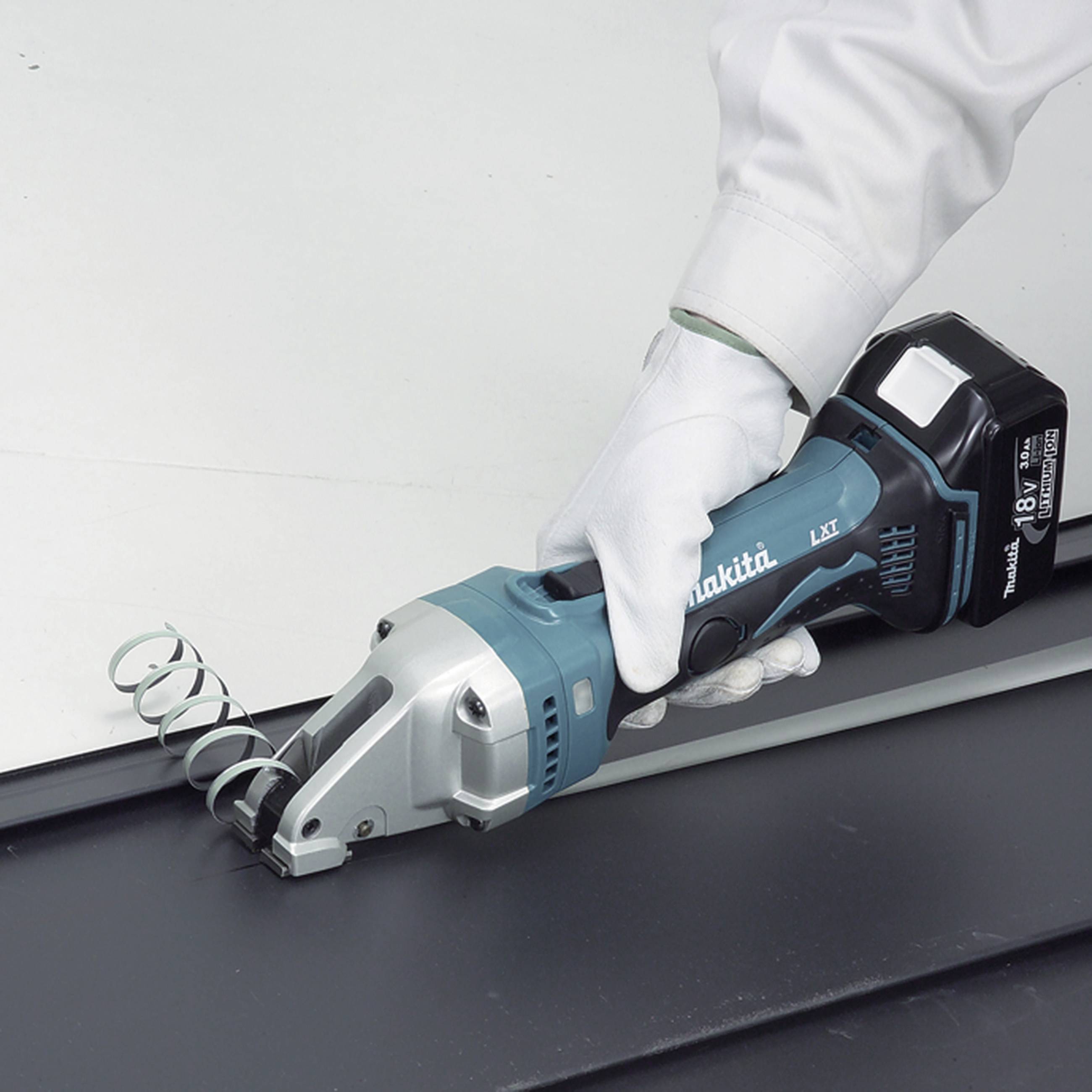 A person is cutting a sheet of metal with a cordless metal shears. The metal shears have a blue handle and a silver cutting edge.