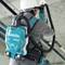 A person is wearing a Makita cordless vacuum on their back and cleaning a pipe in an industrial setting.