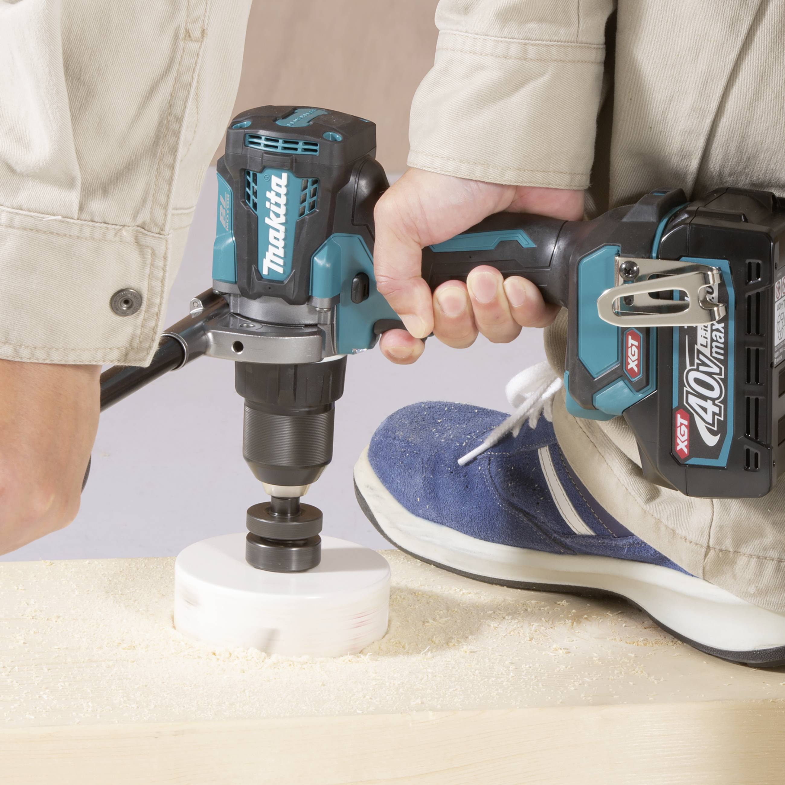 A person is using a blue, cordless drill to bore a circular hole in a piece of wood.