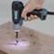 A hand holds a cordless drill and is drilling a hole into a wooden board. Sawdust is scattered around the hole.