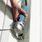 A hand is holding an electric cutting tool, cutting metal along a marked line.