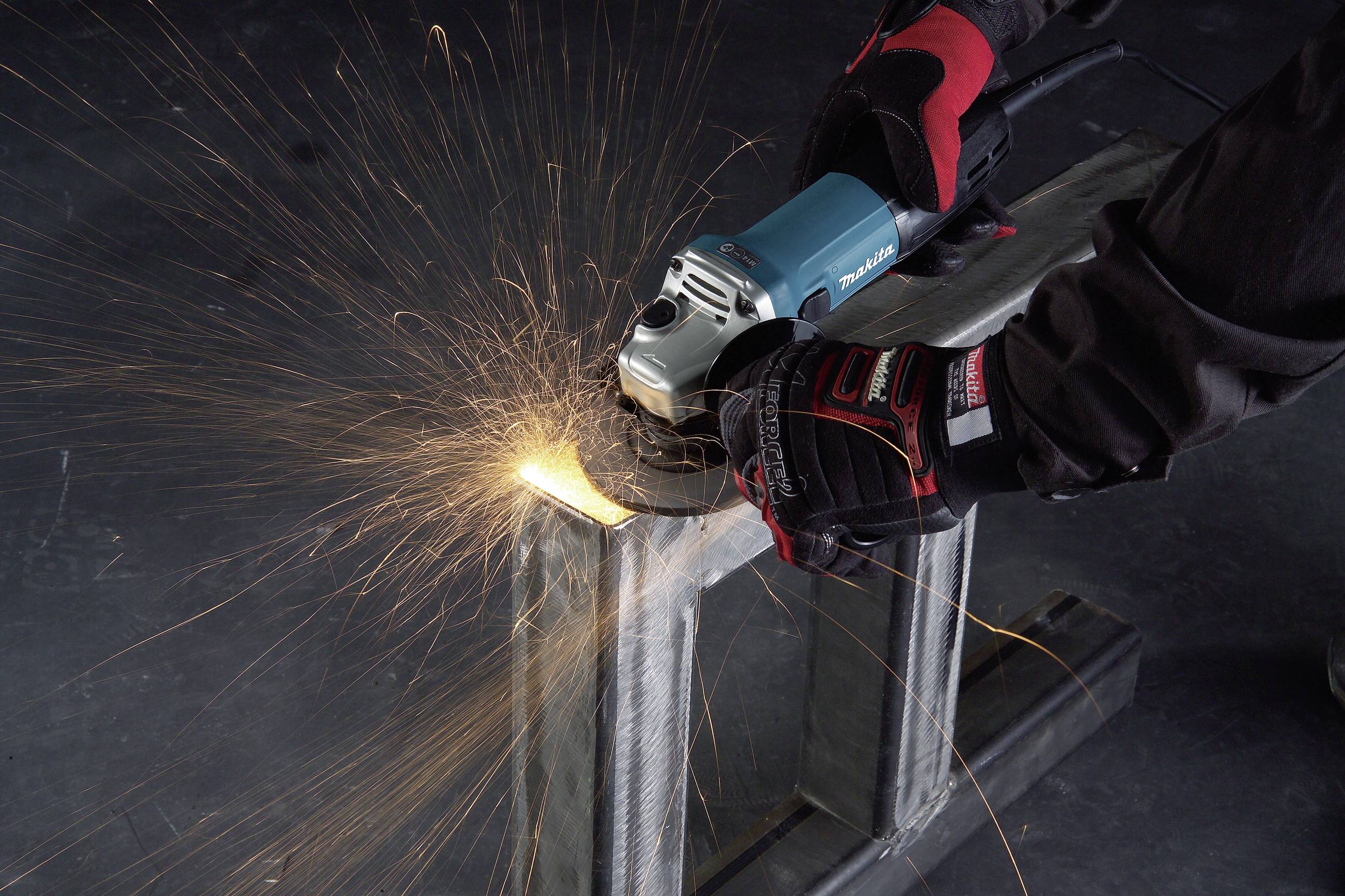 A person is using an angle grinder to grind metal. Sparks are flying during the machining process. They are wearing protective gloves.