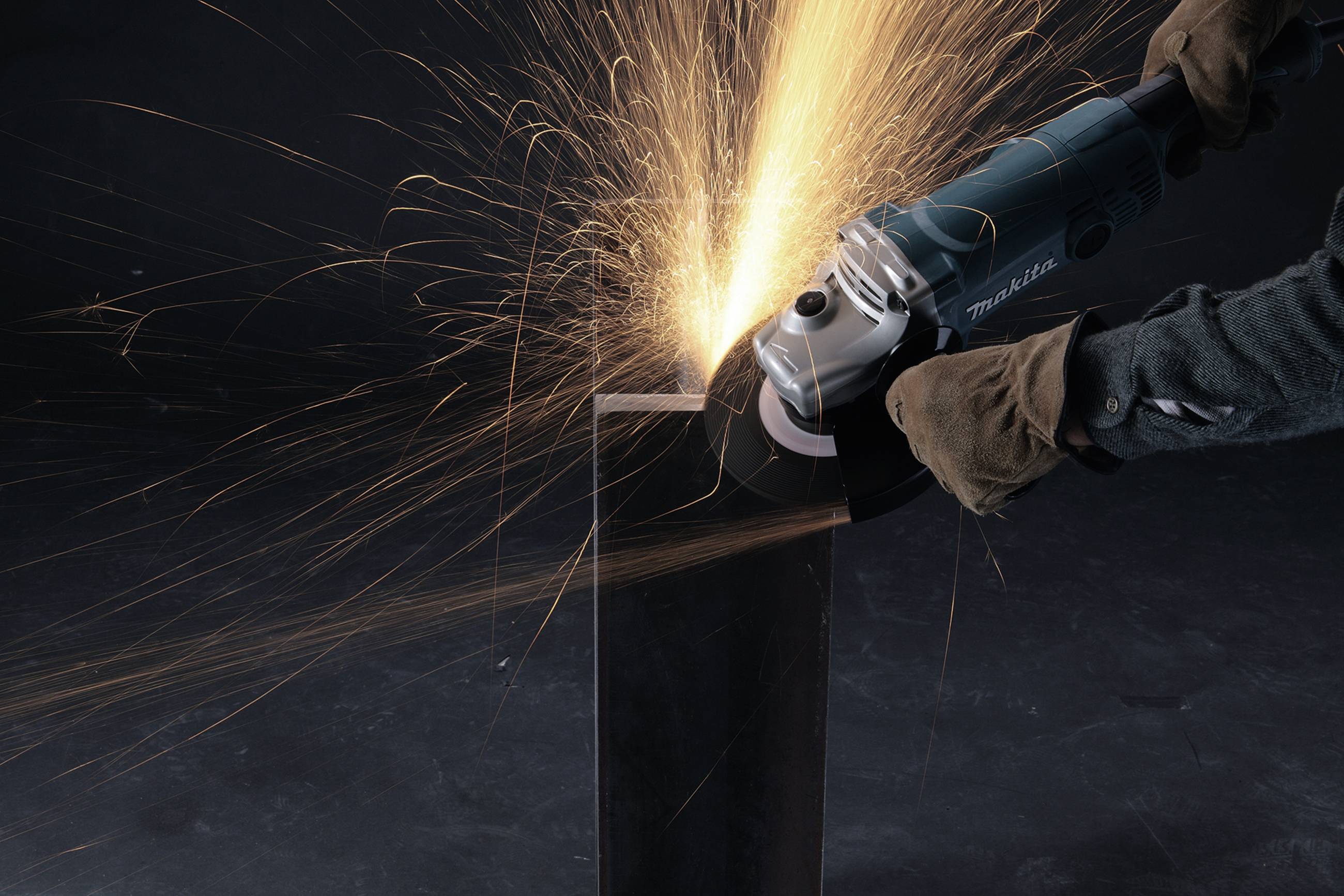 A person is grinding metal with an electric grinding machine. Sparks are flying from the contact point. Safety glasses and gloves are being worn.