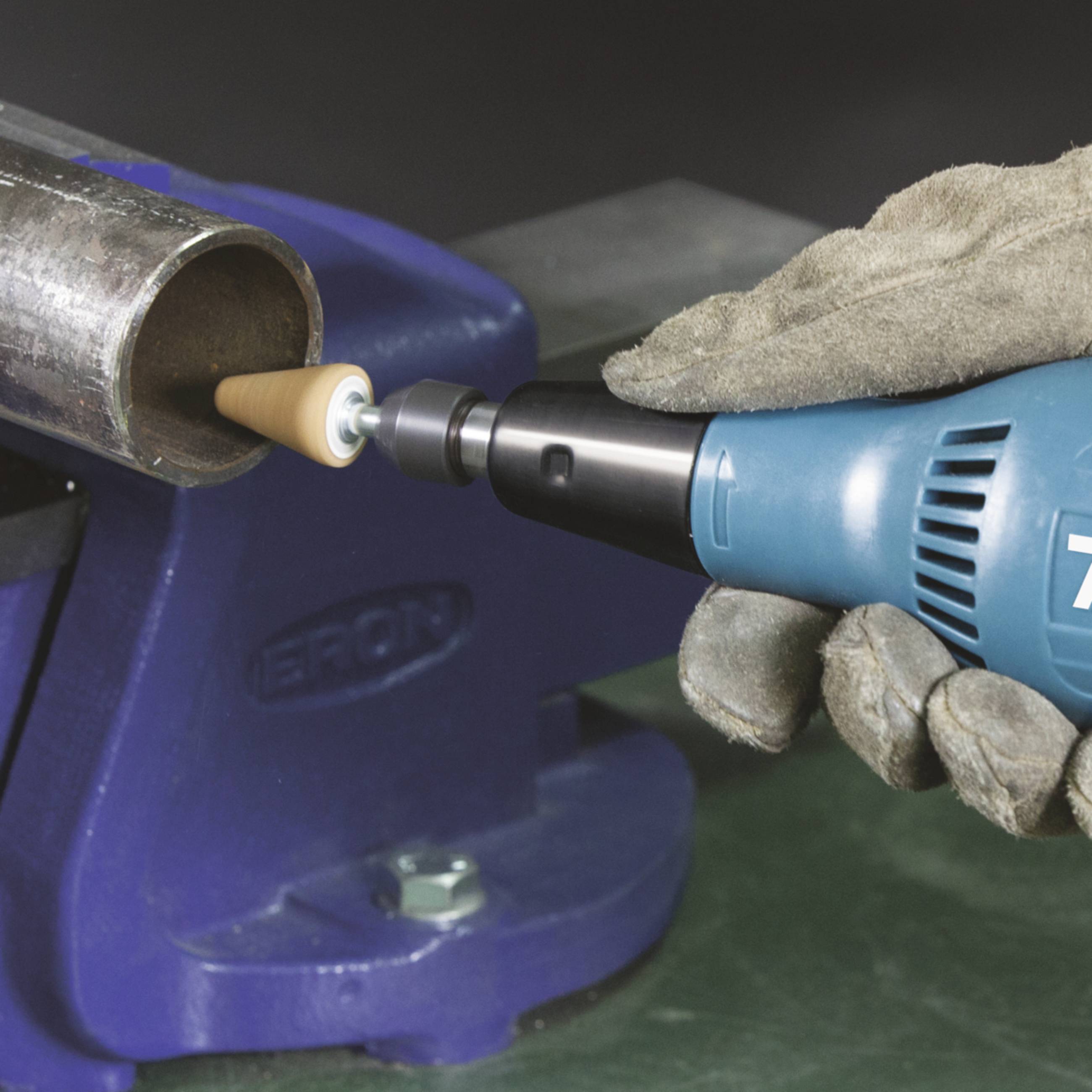 A person wearing work gloves is using an electric polishing machine to polish a piece of metal.