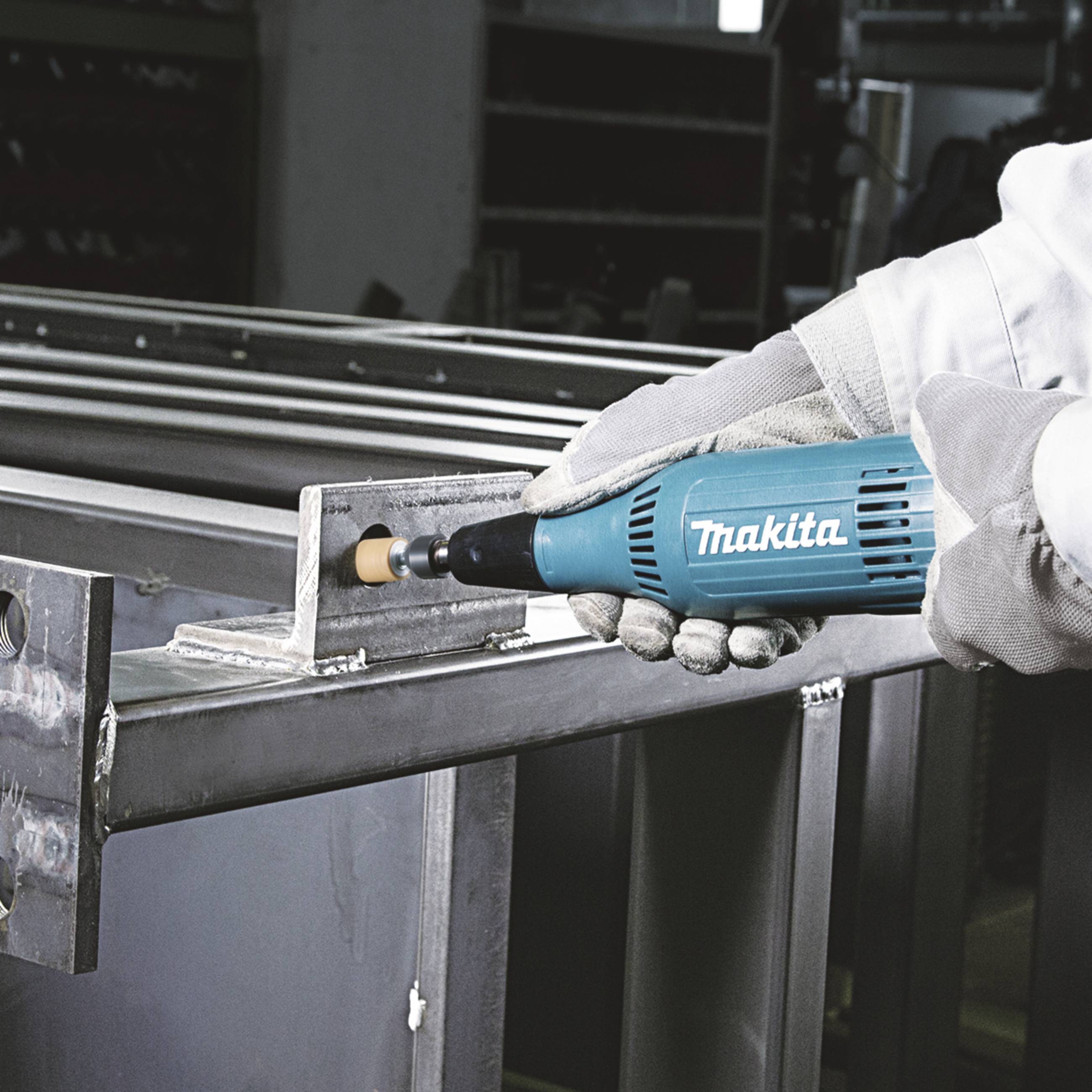 A person is using a light blue Makita tool to grind the metal edges of a steel frame.